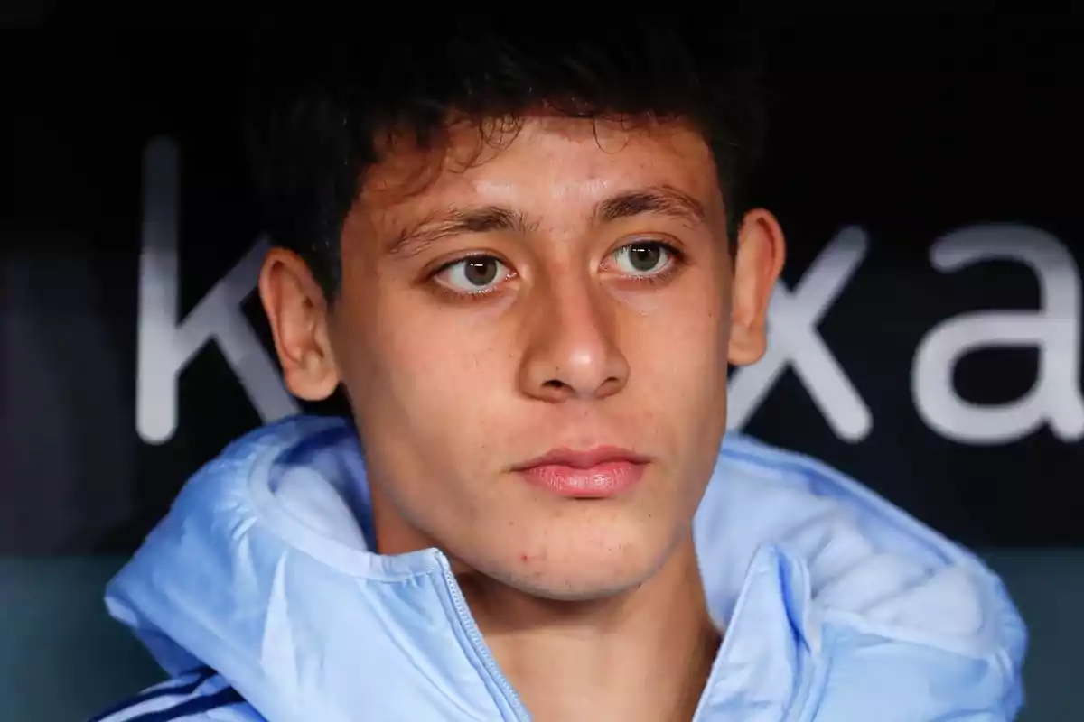 A young man in a light blue jacket looking forward with a serious expression.