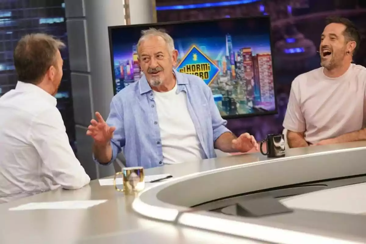 Pablo Motos, Karlos i Joseba Arguiñano conversen i riuen asseguts al voltant d’una taula en un plató de televisió amb el logotip d’‘El Hormiguero’ en una pantalla de fons. Pablo Motos, Karlos i Joseba Arguiñano conversen i riuen asseguts al voltant d’una taula en un plató de televisió amb el logotip d’‘El Hormiguero’ en una pantalla de fons.