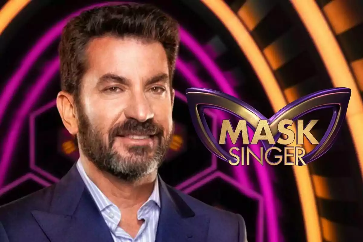 Arturo Valls con barba y traje oscuro aparece frente a un fondo colorido con el logo de "Mask Singer".