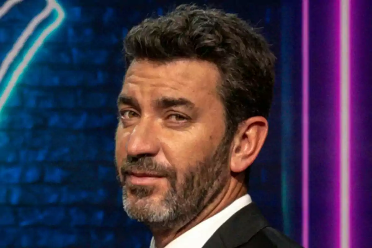 Arturo Valls amb barba i cabell fosc mira cap a la càmera amb una expressió seriosa en un fons fosc amb llums de neó a That's My Jam.