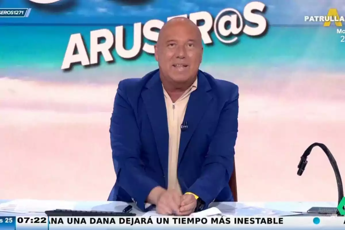 Alfonso Arús amb jaqueta blava i camisa beix està assegut darrere d'un escriptori, amb un micròfon a la dreta i un fons que diu "ARUSER@S". Captura d''Aruser@s' el 25 de juny de 2024