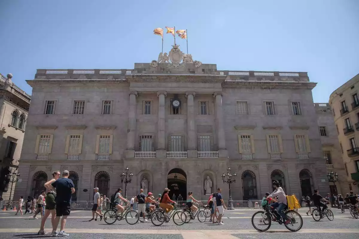 Façana de l'Ajuntament de Barcelona a la plaça Sant Jaume amb diversos ciclistes creuant-la