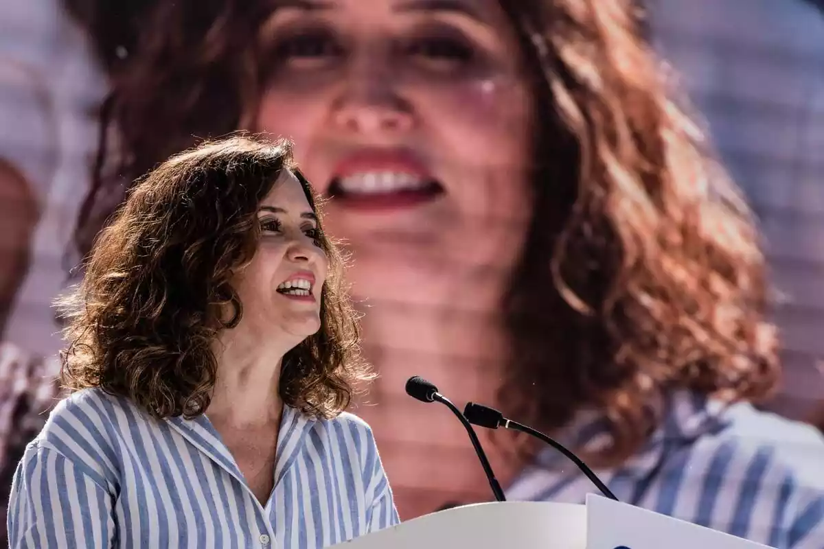 Imatge d'Isabel Díaz Ayuso en un míting del PP amb una pantalla de fons amb la seva pròpia imatge