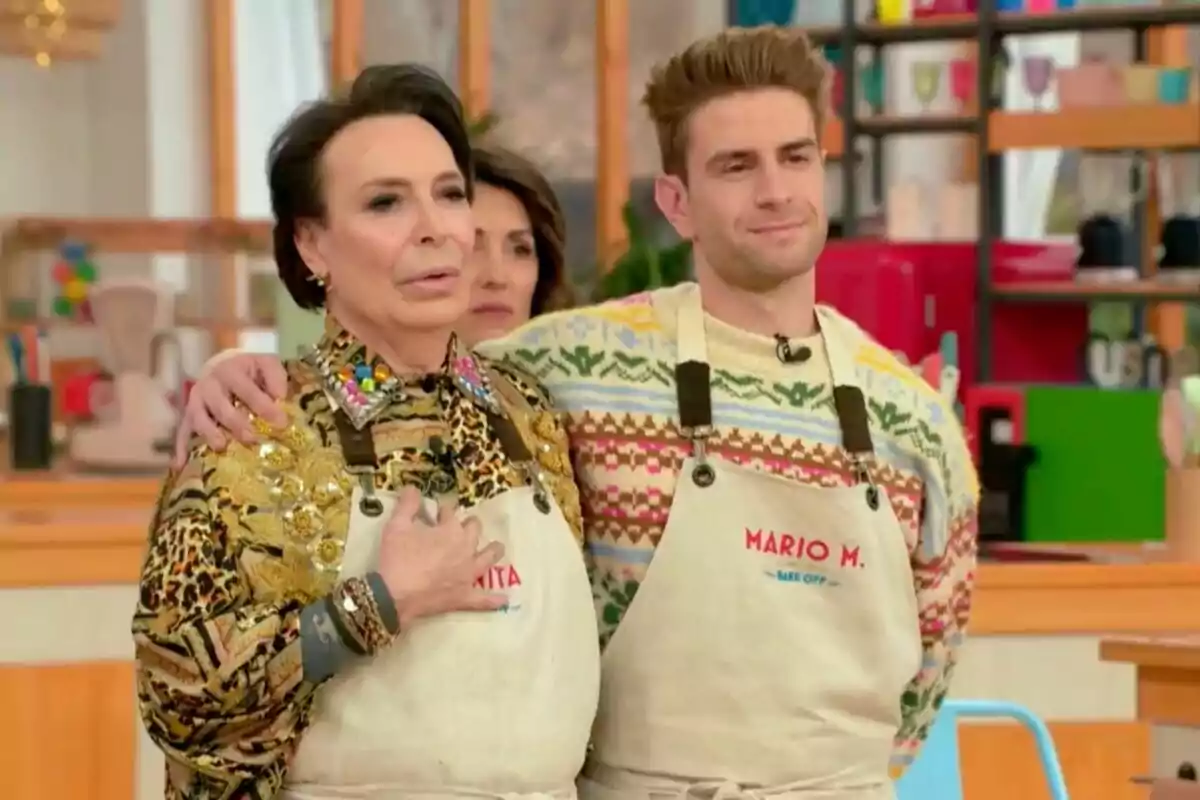 Benita, Maestro Joao, y Mario Marzo con delantales están de pie en un set de cocina, una de ellas tiene el brazo alrededor de la otra en 'Bake off: Famosos al horno'.