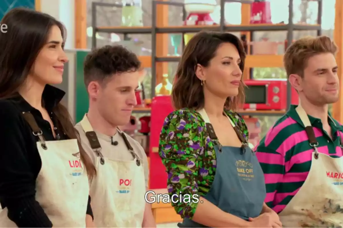 A group of people wearing aprons is standing in a kitchen, possibly participating in a cooking show. Screenshot from 'Bake Off'. A group of people wearing aprons is standing in a kitchen, possibly participating in a cooking show. Screenshot from 'Bake Off'.