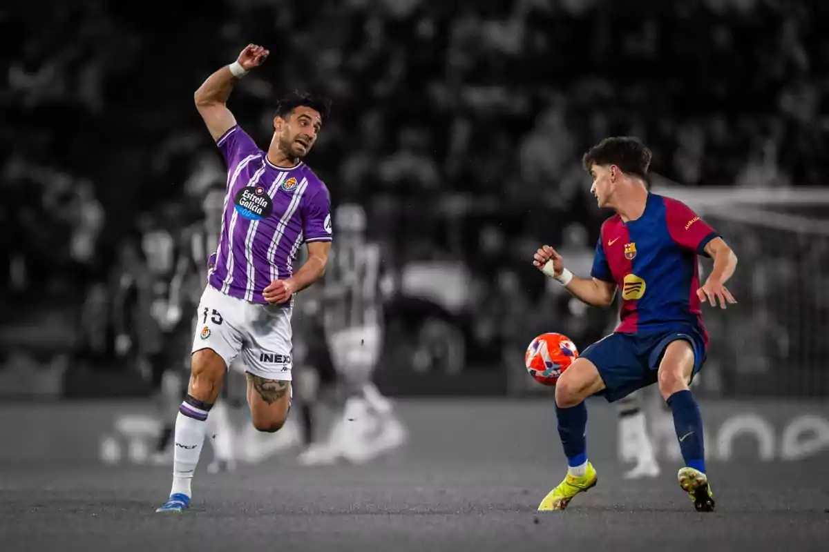 Dos jugadors de futbol en acció durant un partit, un amb uniforme morat i blanc i l'altre amb uniforme blau i vermell en un estadi. Dos jugadors de futbol en acció durant un partit, un amb uniforme morat i blanc i l'altre amb uniforme blau i vermell en un estadi.