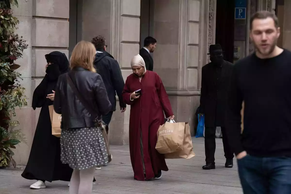 Diverses persones caminant pel carrer de Barcelona, dues són dones amb vel i bruka