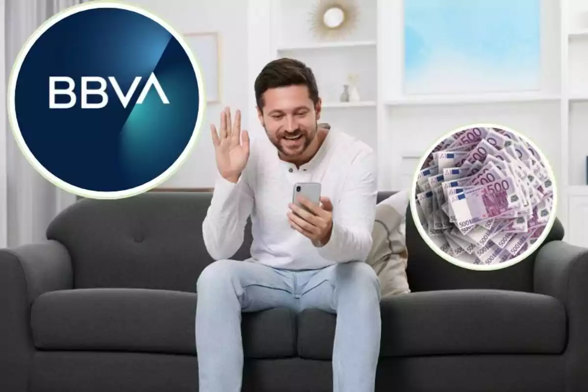 Un hombre sentado en un sofá gris, sonriendo y saludando mientras sostiene un teléfono móvil, con el logotipo de BBVA a la izquierda y una pila de billetes de 500 euros a la derecha.