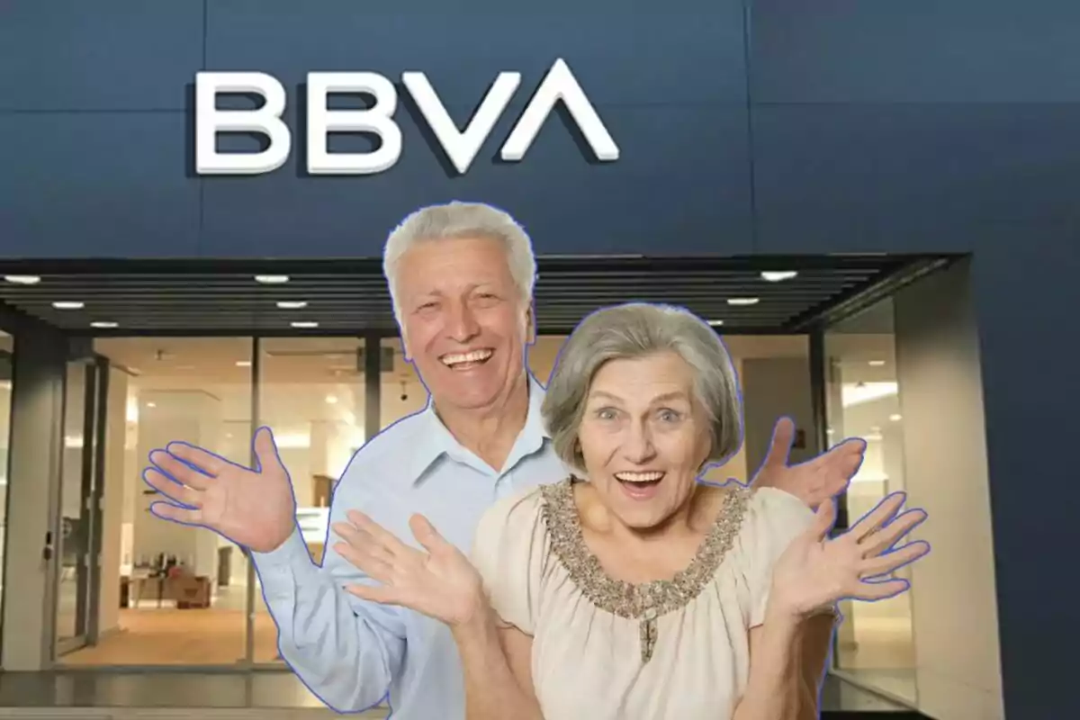 Una parella de persones grans somriu i aixeca les mans davant d'una sucursal del banc BBVA.