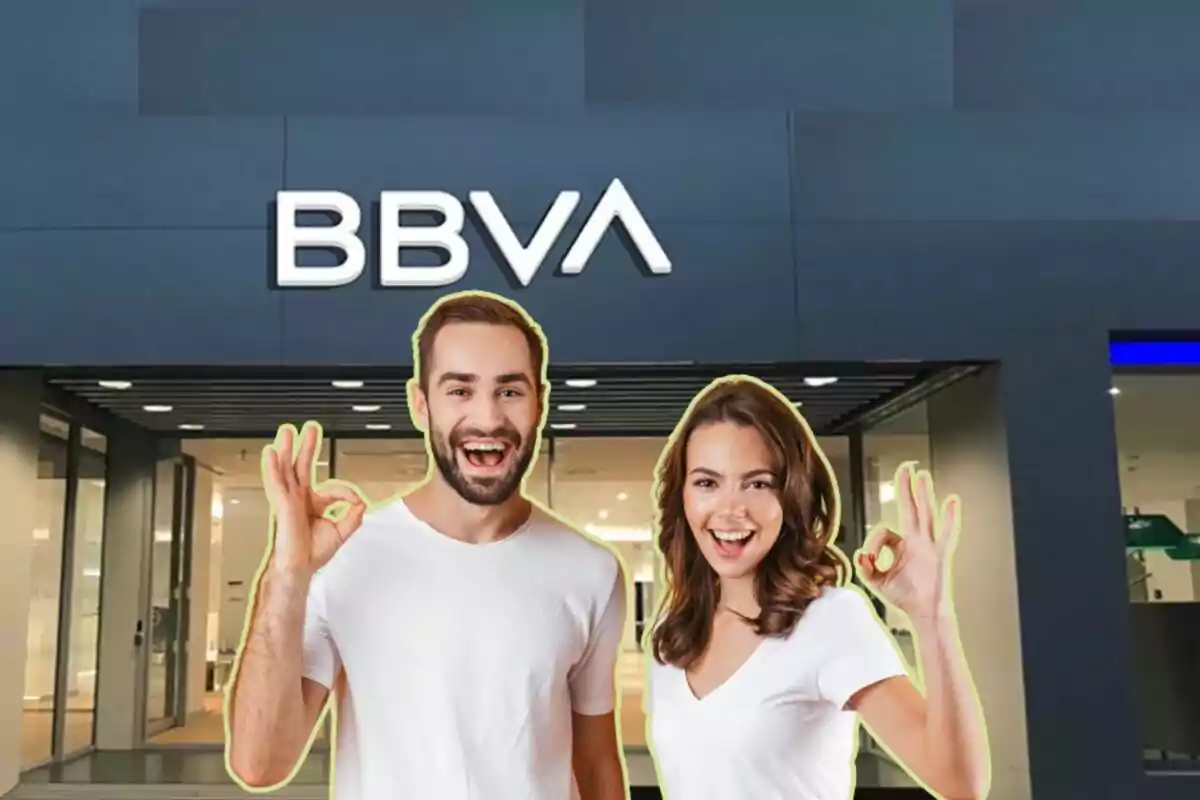 Dues persones somrients fent el gest de “OK” davant d'una sucursal del banc BBVA.