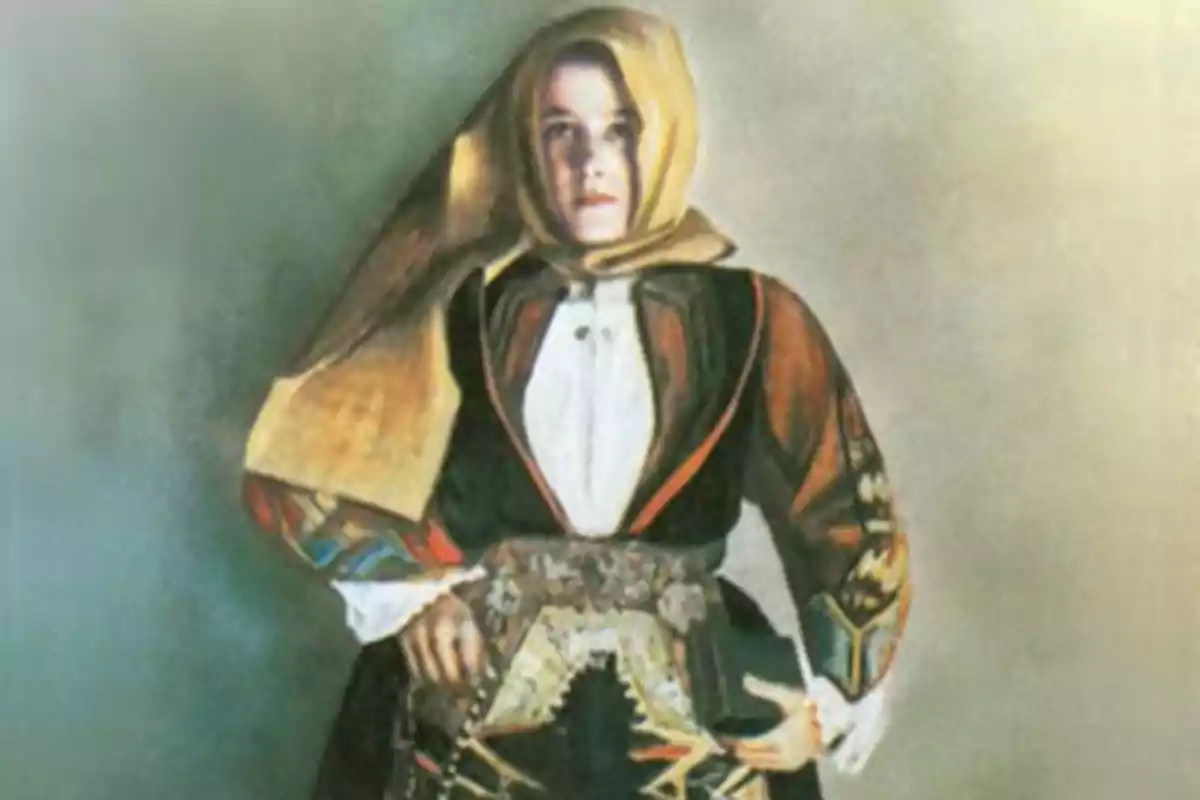 Una persona vestida amb un vestit tradicional que inclou un mocador al cap i una jaqueta decorada, posant amb les mans a la cintura. Una persona vestida amb un vestit tradicional que inclou un mocador al cap i una jaqueta decorada, posant amb les mans a la cintura.