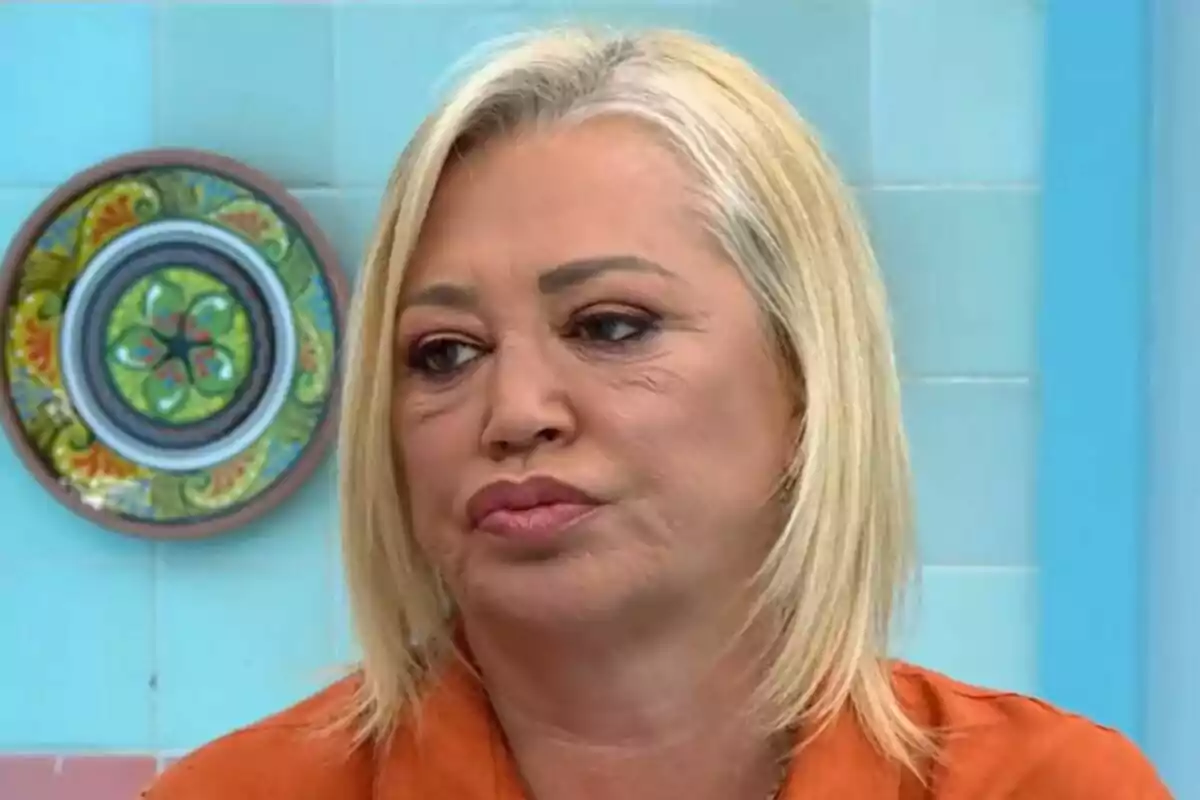 Belén Esteban de cabell ros i expressió seriosa en un entorn amb rajoles blaves i un plat decoratiu a la paret a La Família de la Tele.