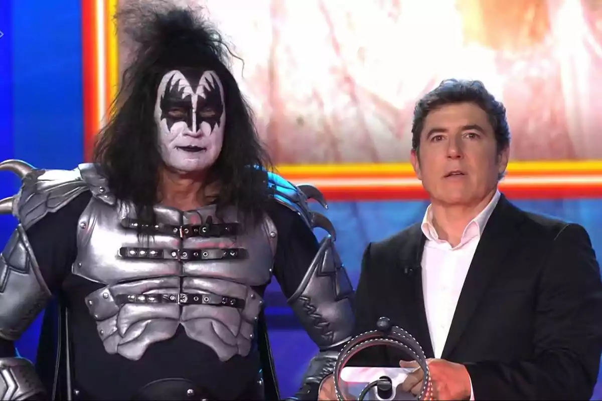 Bertín Osborne i Manel Fuentes en un escenari, una vestida amb un vestit metàl·lic i maquillatge cridaner, i l'altra amb vestit formal a Tu Cara Me Suena.