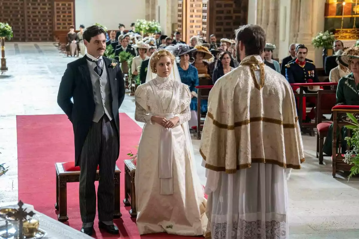 Arturo Sancho i Ana Garcés vestits d'època està dret davant d'un sacerdot en una cerimònia de casament a una església, envoltats de convidats asseguts, a La Promesa.