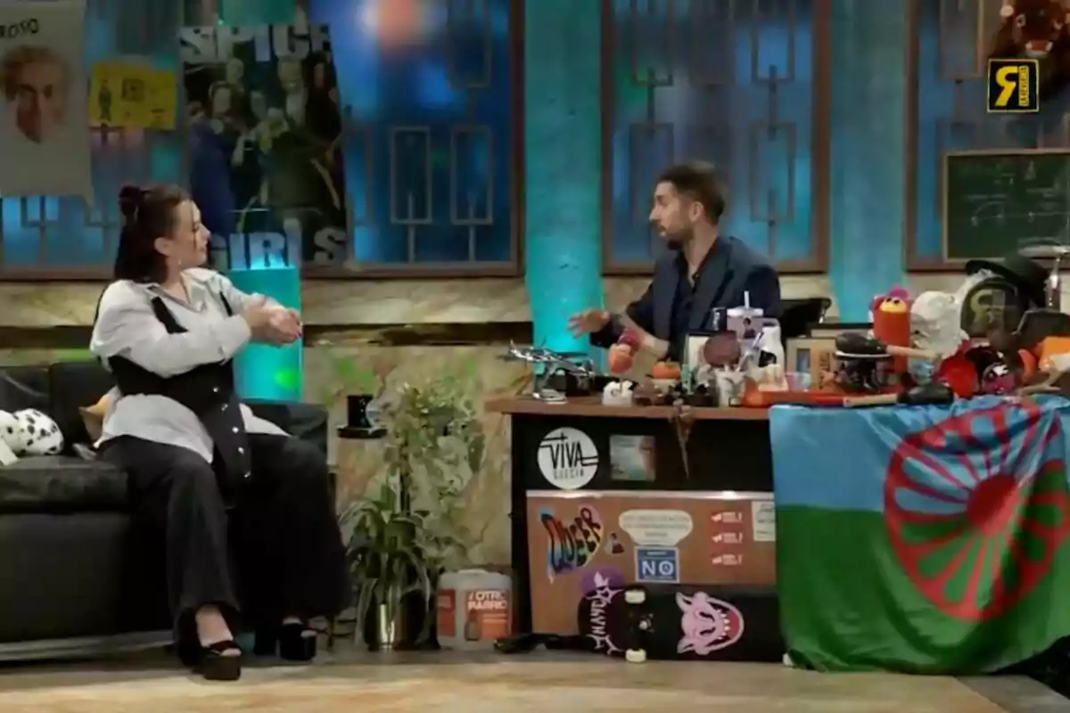 Lia Kali i David Broncano conversen en un plató de televisió decorat amb cartells i objectes diversos, incloent-hi una bandera i un monopatí a 'La Revuelta'. Lia Kali i David Broncano conversen en un plató de televisió decorat amb cartells i objectes diversos, incloent-hi una bandera i un monopatí a 'La Revuelta'.