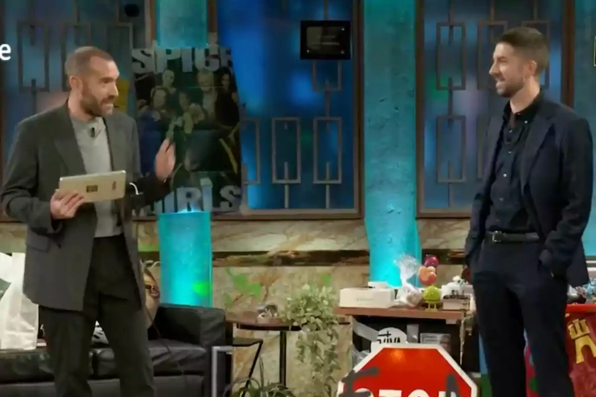Jorge Ponce i David Broncano conversen en un plató de televisió decorat amb cartells i objectes variats, un d'ells sosté una tauleta mentre l'altre somriu. Jorge Ponce i David Broncano conversen en un plató de televisió decorat amb cartells i objectes variats, un d'ells sosté una tauleta mentre l'altre somriu.