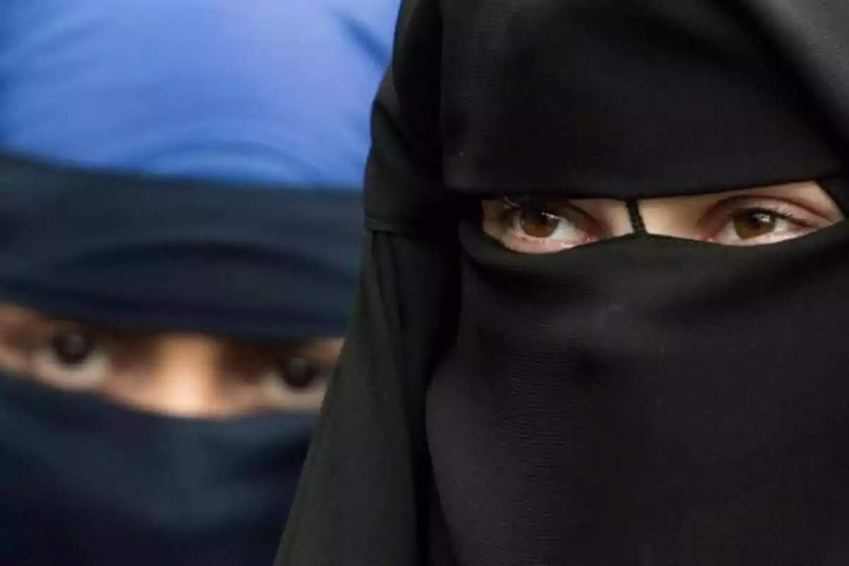 Dues persones amb niqab, una en primer pla amb un niqab negre i una altra al fons amb un niqab blau.