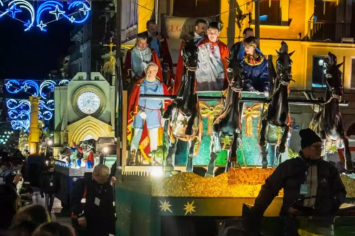 Un desfile nocturno con carrozas iluminadas y figuras de caballos en una calle decorada con luces festivas.