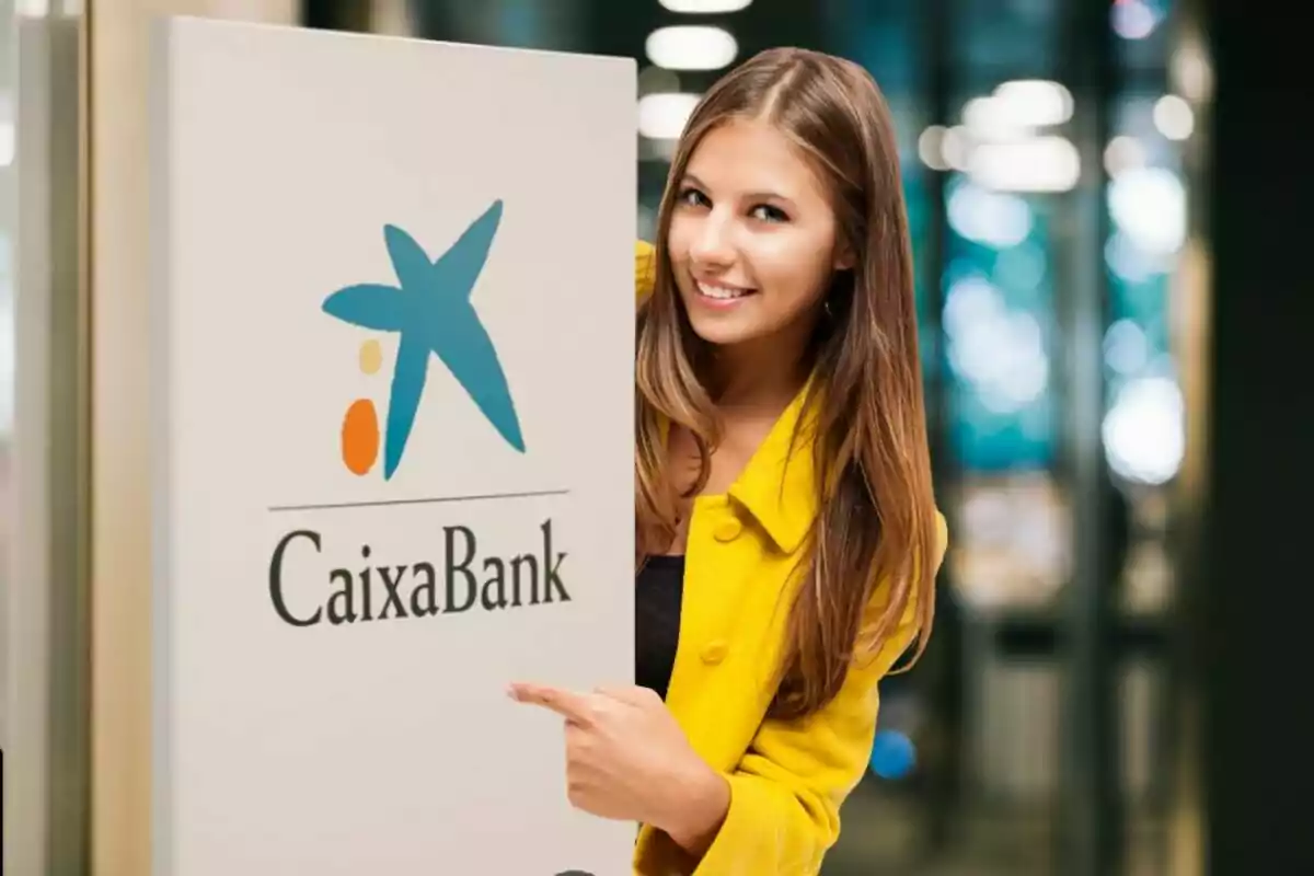 Una dona amb una jaqueta groga somriu i assenyala un cartell de CaixaBank.