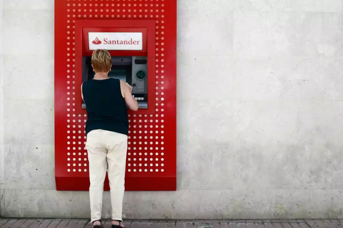 Cajero exterior del Banco Santander con una mujer de espaldas con una blusa negra y pantalones blancos