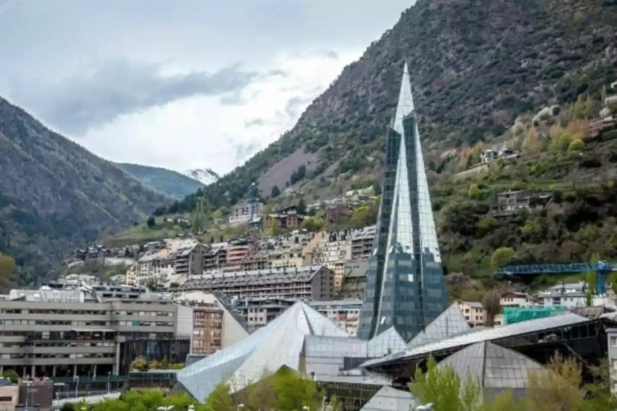 Vista de un edificio moderno con una estructura de cristal en un entorno montañoso con vegetación y casas en la ladera.