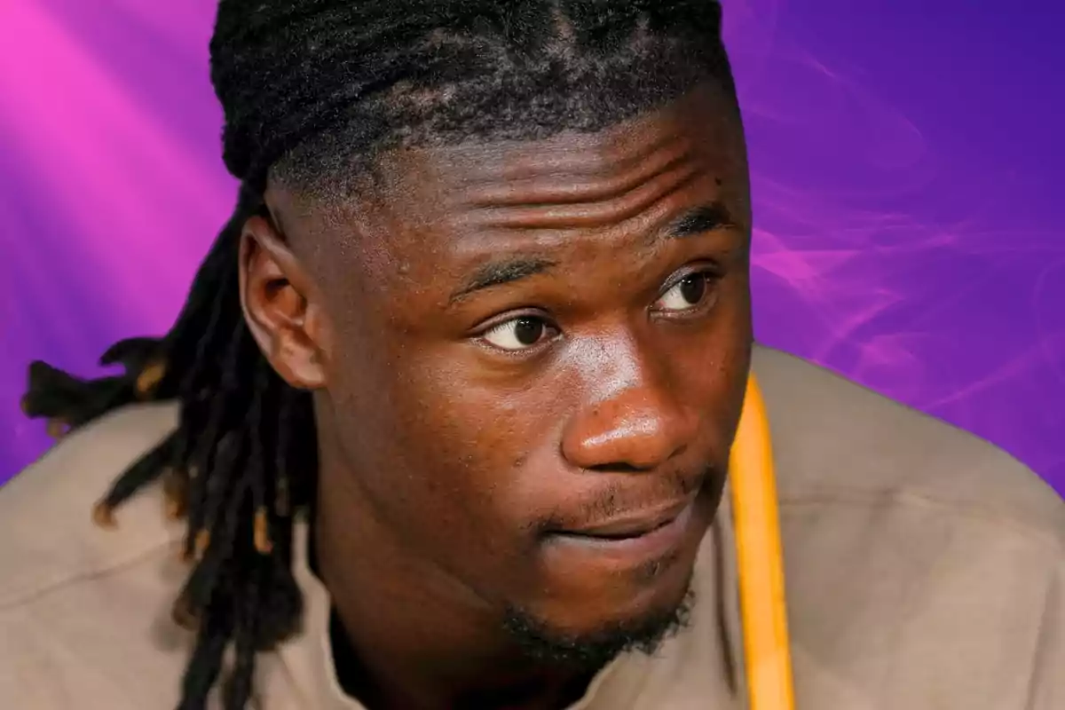 A man with dreadlocks and a pensive expression against a purple background.