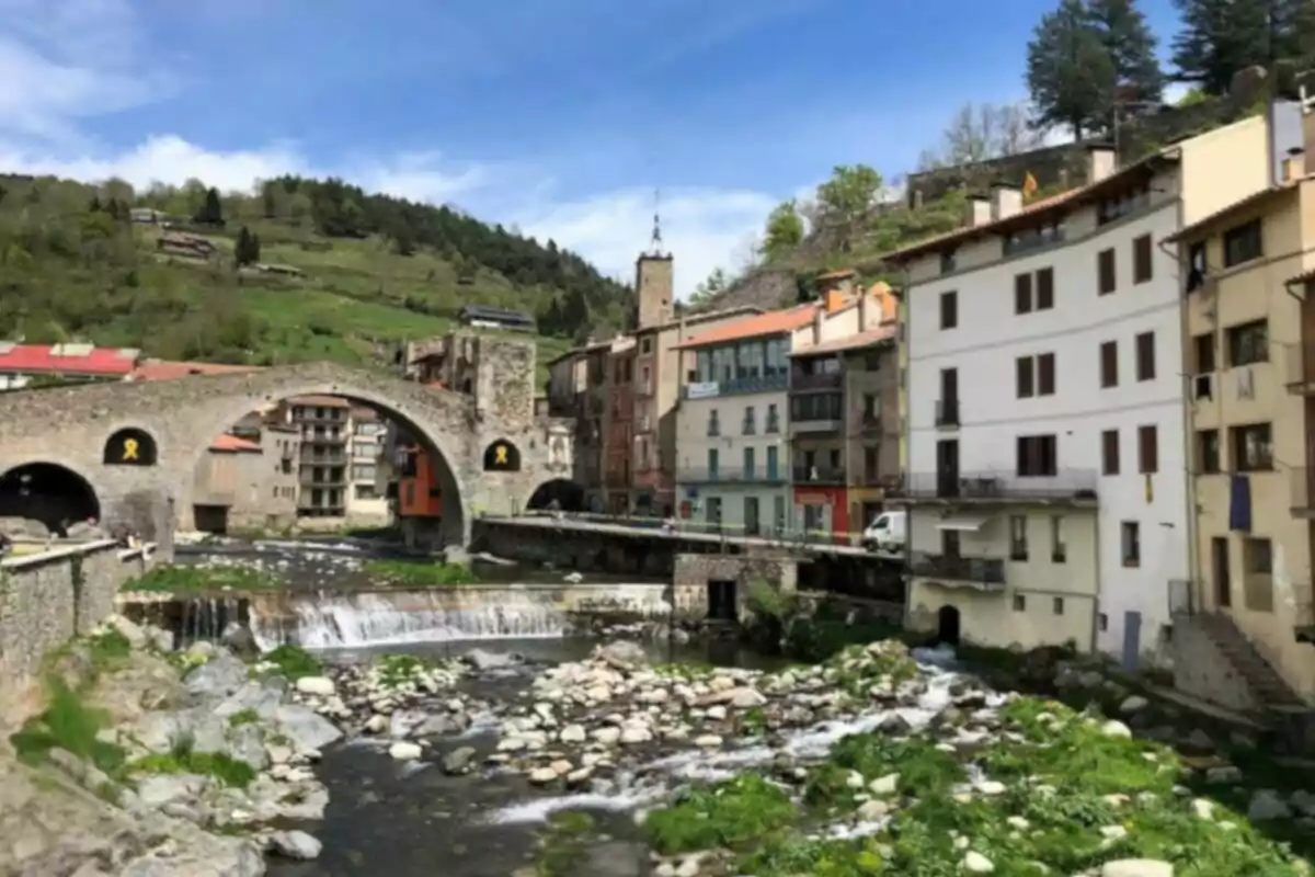 Un puente de piedra medieval cruza un río rodeado de casas coloridas y colinas verdes.