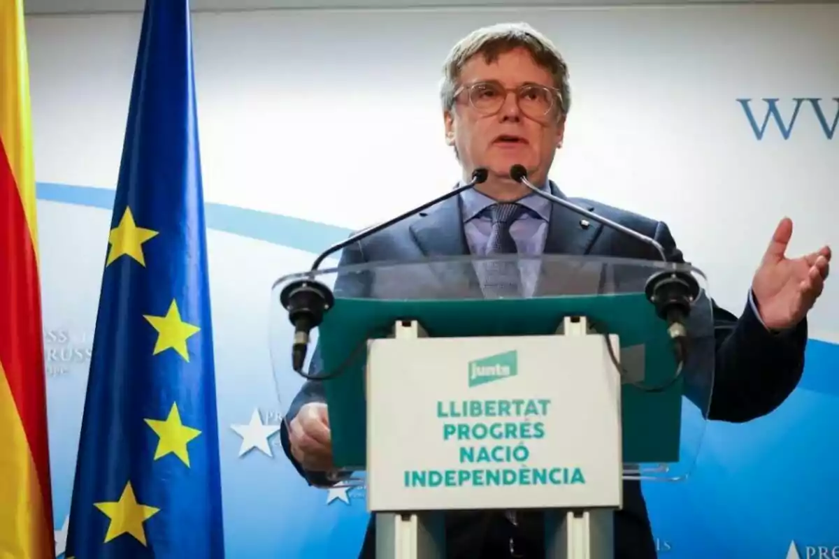 A man speaking at a podium with the flags of the European Union and Spain beside him.