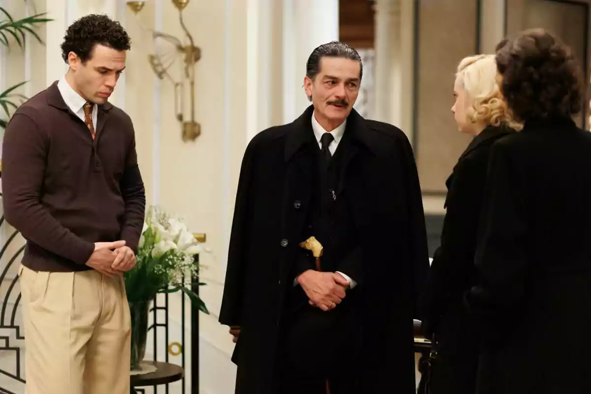 Jesús Mosquera, Carles Sanjaime and two women talk in an elegant interior, one of them wears a black coat and holds a hat in the modern one.