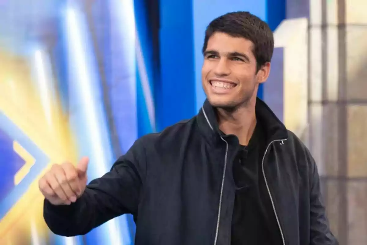 Carlos Alcaraz somrient i aixecant el polze a El Hormiguero amb llums de fons.