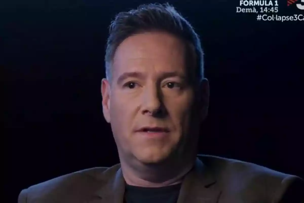 Carlos Latre de cabell curt i expressió seriosa assegut davant d’un fons fosc a Col·lapse
