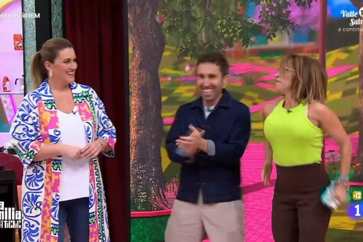 Carlota Corredera, Aitor Albizua i María Patiño somriuen i aplaudeixen en un plató de televisió acolorit amb un fons d'arbres i camins a La Família de la Tele. Carlota Corredera, Aitor Albizua i María Patiño somriuen i aplaudeixen en un plató de televisió acolorit amb un fons d'arbres i camins a La Família de la Tele.