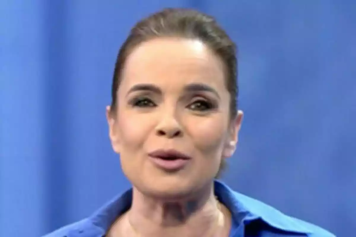 Carme Chaparro con cabello recogido y camisa azul sobre un fondo azul en Informativos Telecinco.