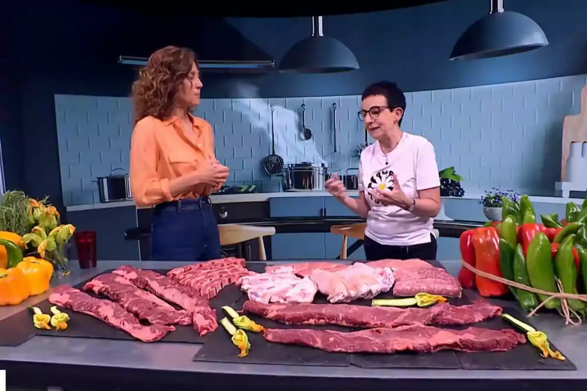 Helena García Meleroo i Carme Ruscalleda conversen en una cuina moderna amb una taula plena de diferents talls de carn i verdures fresques a Tot es Mou.