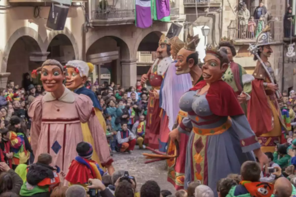 Un desfile de figuras gigantes con trajes coloridos en una plaza llena de espectadores.