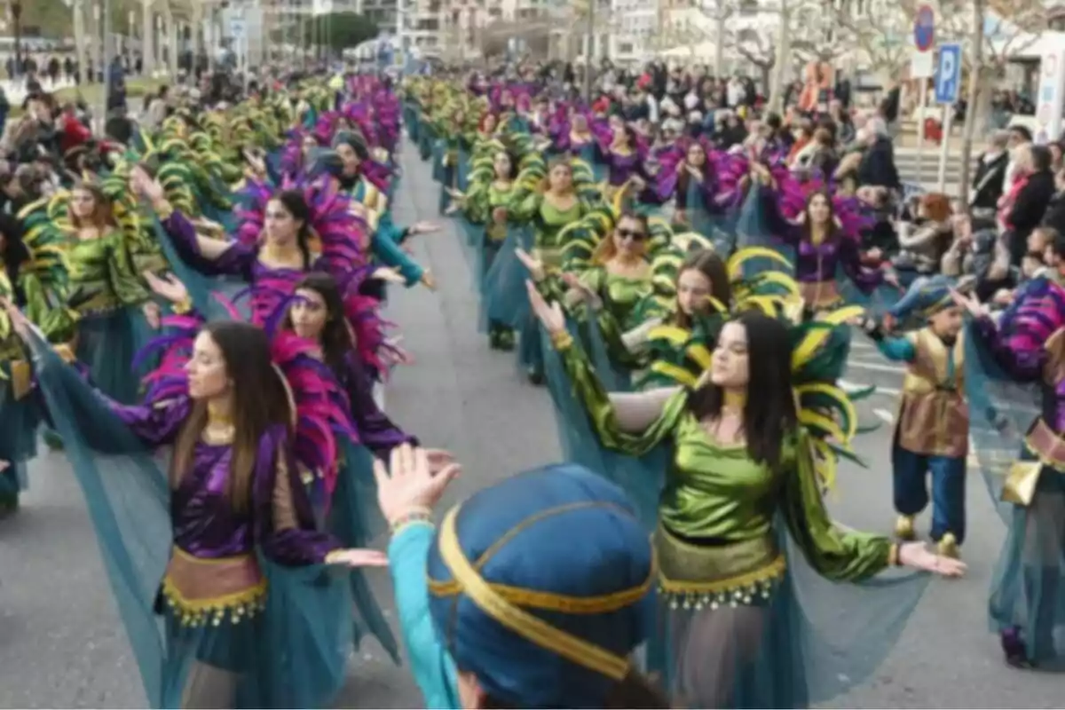 Un grupo de personas vestidas con trajes coloridos y plumas participa en un desfile en la calle mientras el público observa.