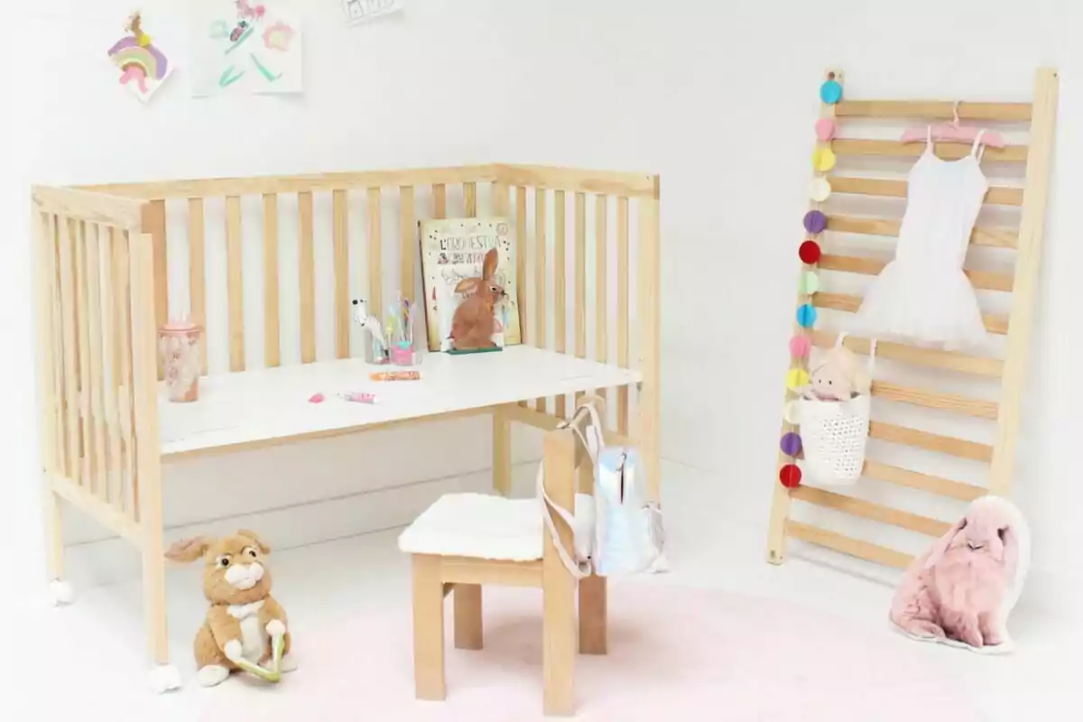 Una habitación infantil con una cuna de madera que se usa como escritorio, una silla pequeña, juguetes de peluche, libros, dibujos en la pared y una escalera de madera decorada con una guirnalda de colores y un vestido blanco. Una habitación infantil con una cuna de madera que se usa como escritorio, una silla pequeña, juguetes de peluche, libros, dibujos en la pared y una escalera de madera decorada con una guirnalda de colores y un vestido blanco.
