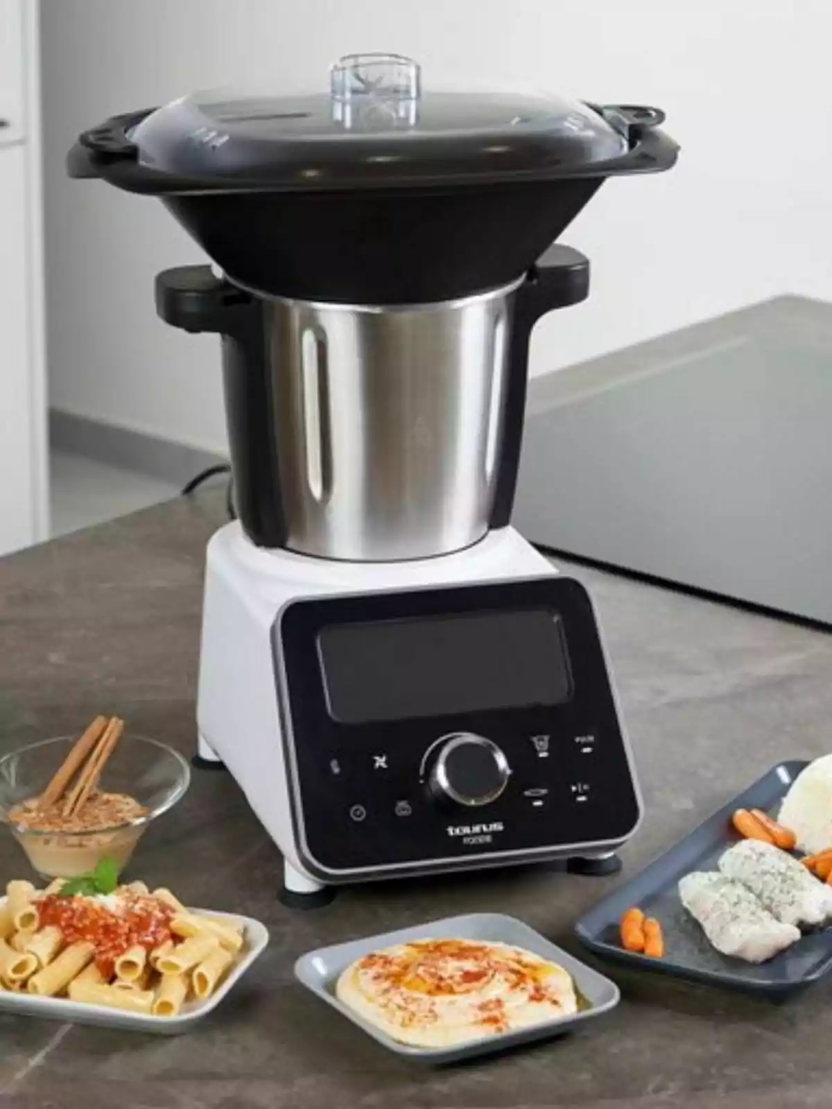 A multifunctional kitchen blender on a countertop next to dishes of food like pasta, hummus, and fish with vegetables. A multifunctional kitchen blender on a countertop next to dishes of food like pasta, hummus, and fish with vegetables.