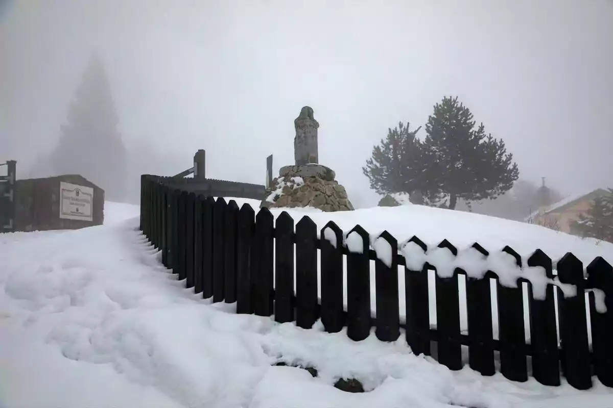 Una estàtua de pedra en un paisatge nevat envoltada per una tanca de fusta fosca amb arbres i boira al fons. Una estàtua de pedra en un paisatge nevat envoltada per una tanca de fusta fosca amb arbres i boira al fons.