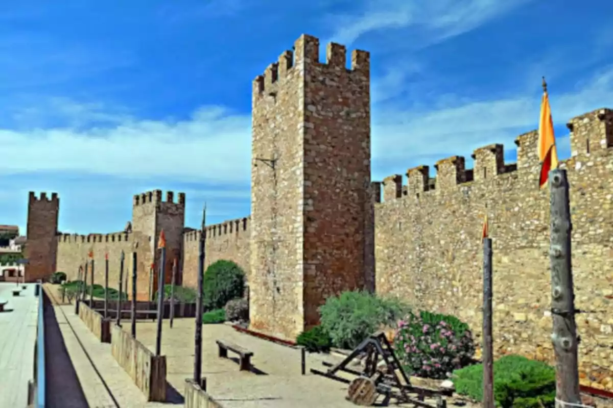 Walls of a medieval castle with towers and flags under a blue sky.