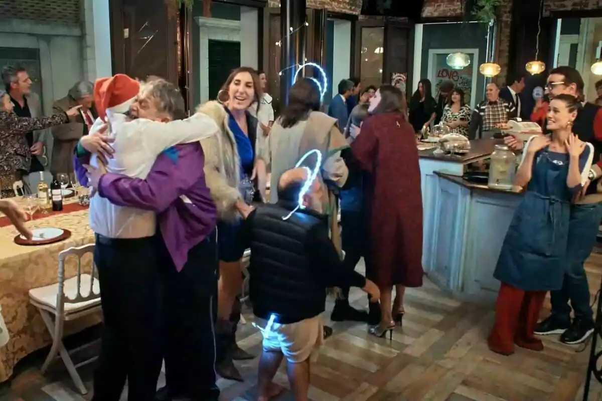 Un grup de persones celebra en una festa, algunes s'abracen i d'altres conversen animadament al voltant d'una taula decorada a La que s'acosta.