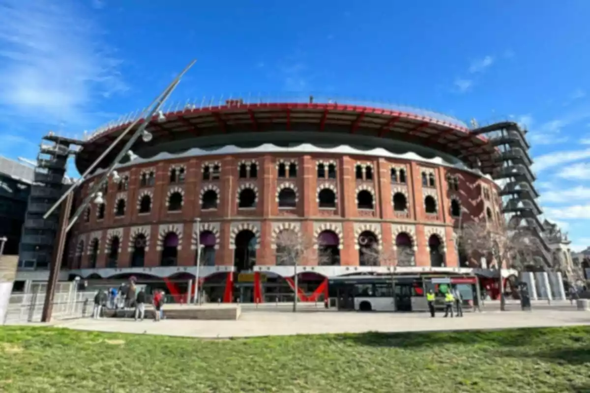 Un edifici circular de maó amb múltiples arcs i detalls arquitectònics, envoltat de persones i un autobús a la part frontal, sota un cel blau. Un edifici circular de maó amb múltiples arcs i detalls arquitectònics, envoltat de persones i un autobús a la part frontal, sota un cel blau.