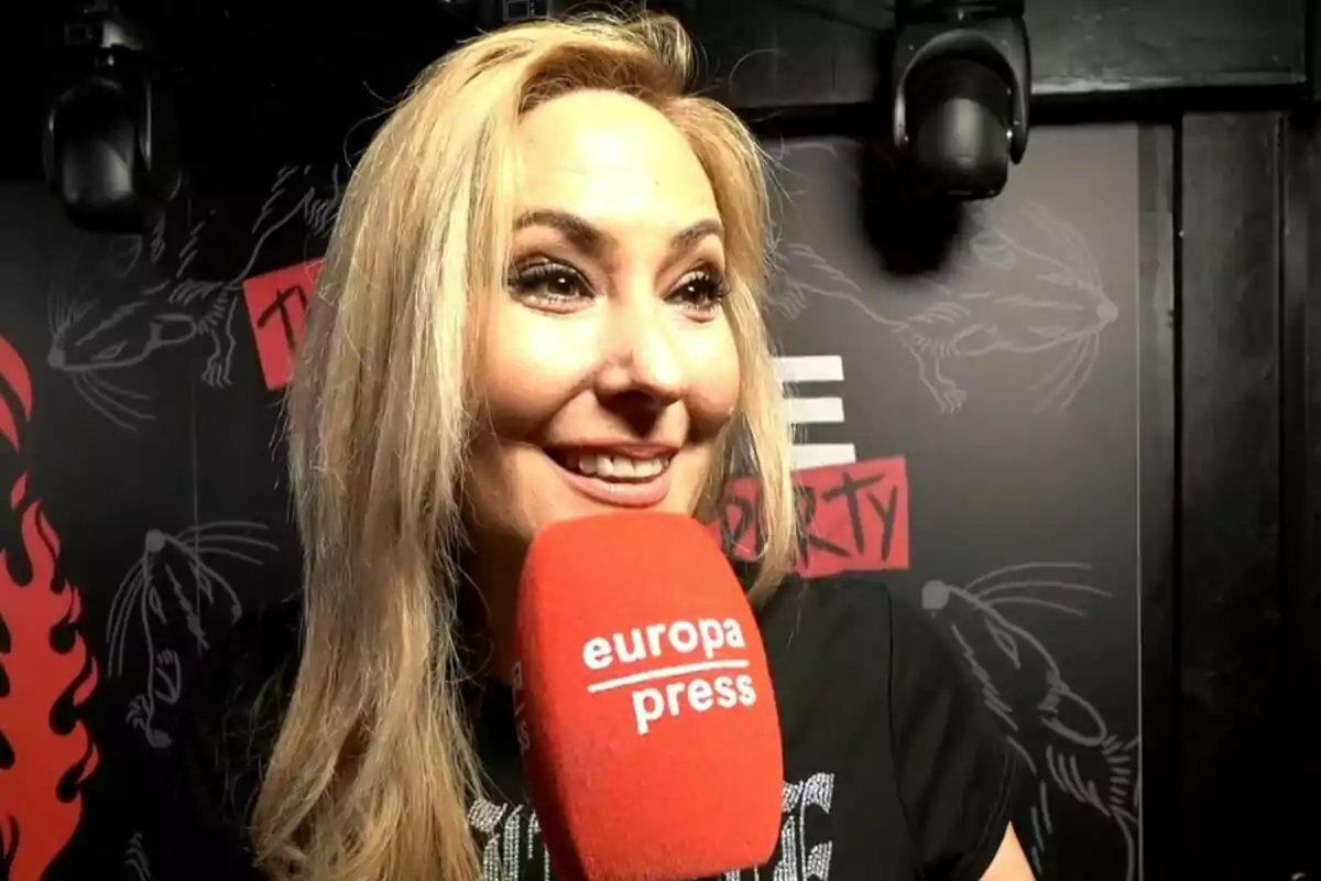 Chayo Mohedano smiling while holding a red Europa Press microphone at an event with a dark background.