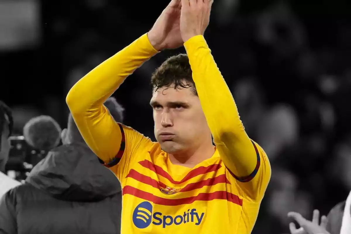 A soccer player in a yellow and red uniform claps with his hands above his head.