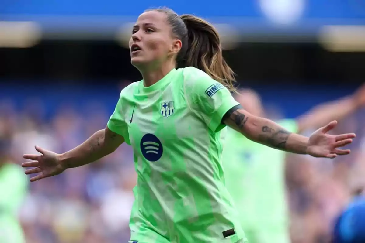 Futbolista amb uniforme verd celebrant un gol amb els braços estesos en un estadi Futbolista amb uniforme verd celebrant un gol amb els braços estesos en un estadi