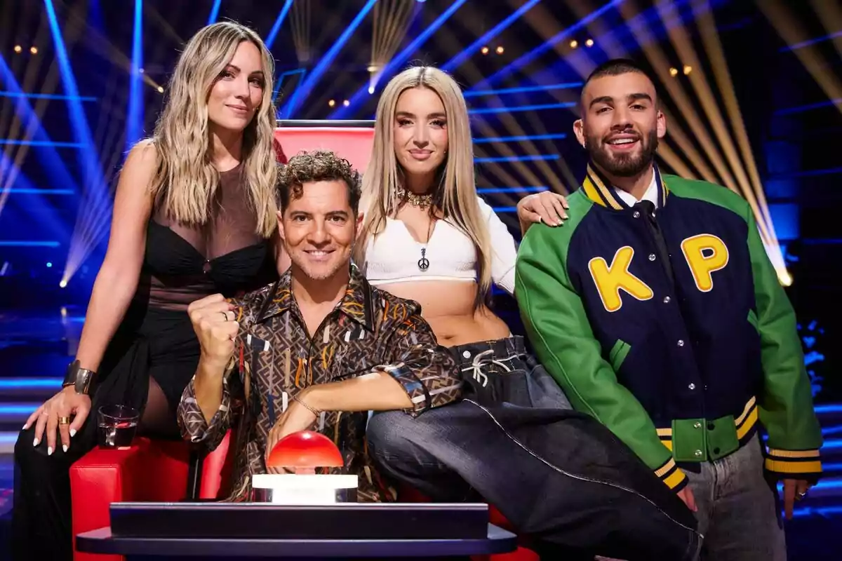 Edurne, David Bisbal, Lola Índigo i Manuel Turizo posen junts en un escenari il·luminat amb llums blaves i grogues, una d'elles està asseguda en una cadira vermella amb un botó gran davant d'ells a La Voz Kids. Edurne, David Bisbal, Lola Índigo i Manuel Turizo posen junts en un escenari il·luminat amb llums blaves i grogues, una d'elles està asseguda en una cadira vermella amb un botó gran davant d'ells a La Voz Kids.
