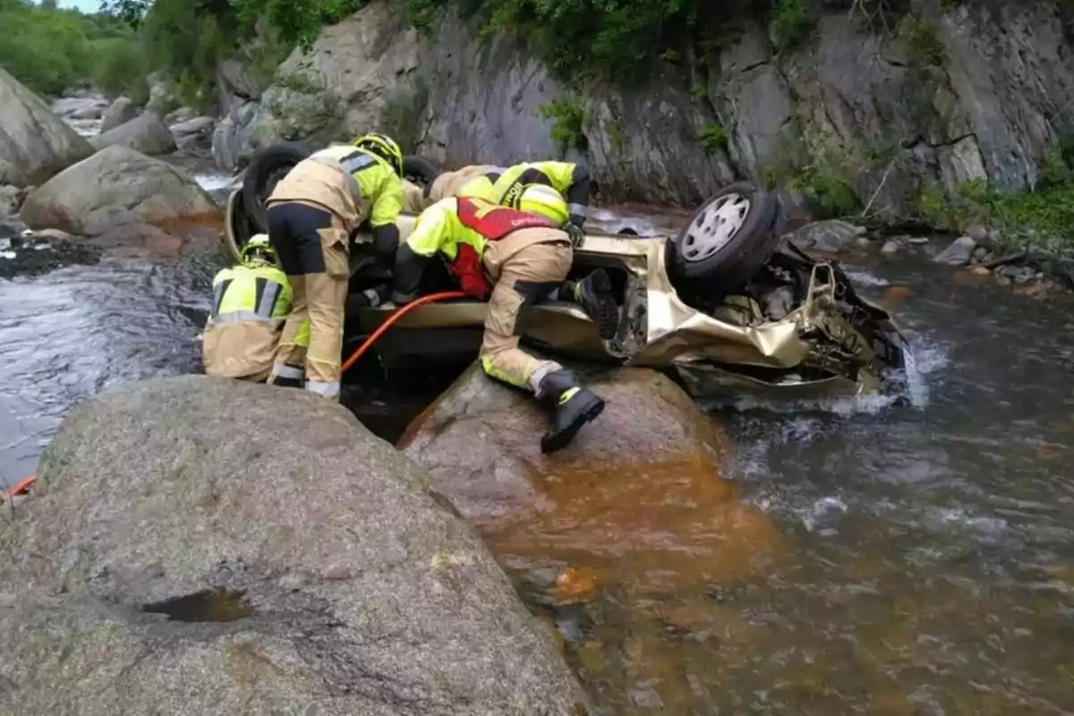 Bombers rescaten una persona d'un automòbil bolcat en una riera entre roques.