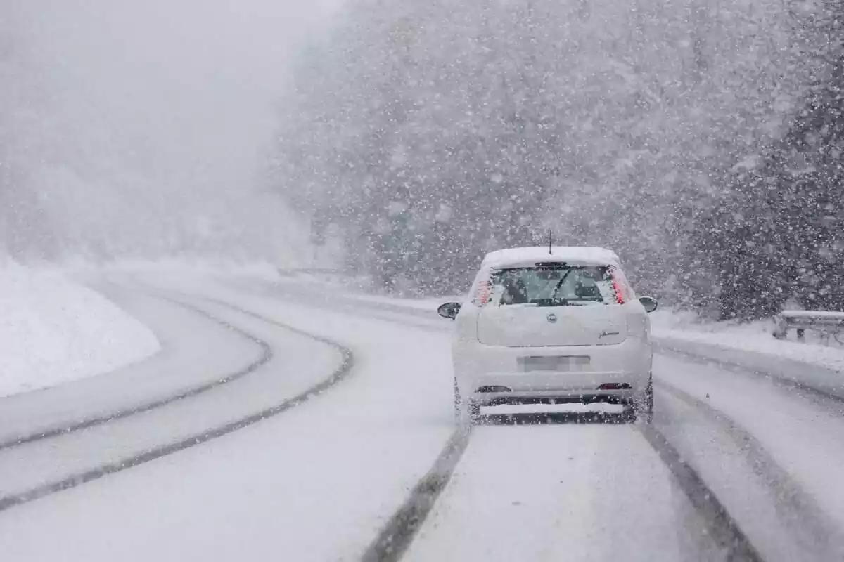 Un cotxe circulant al mig de la nevada per una carretera força plena de neu