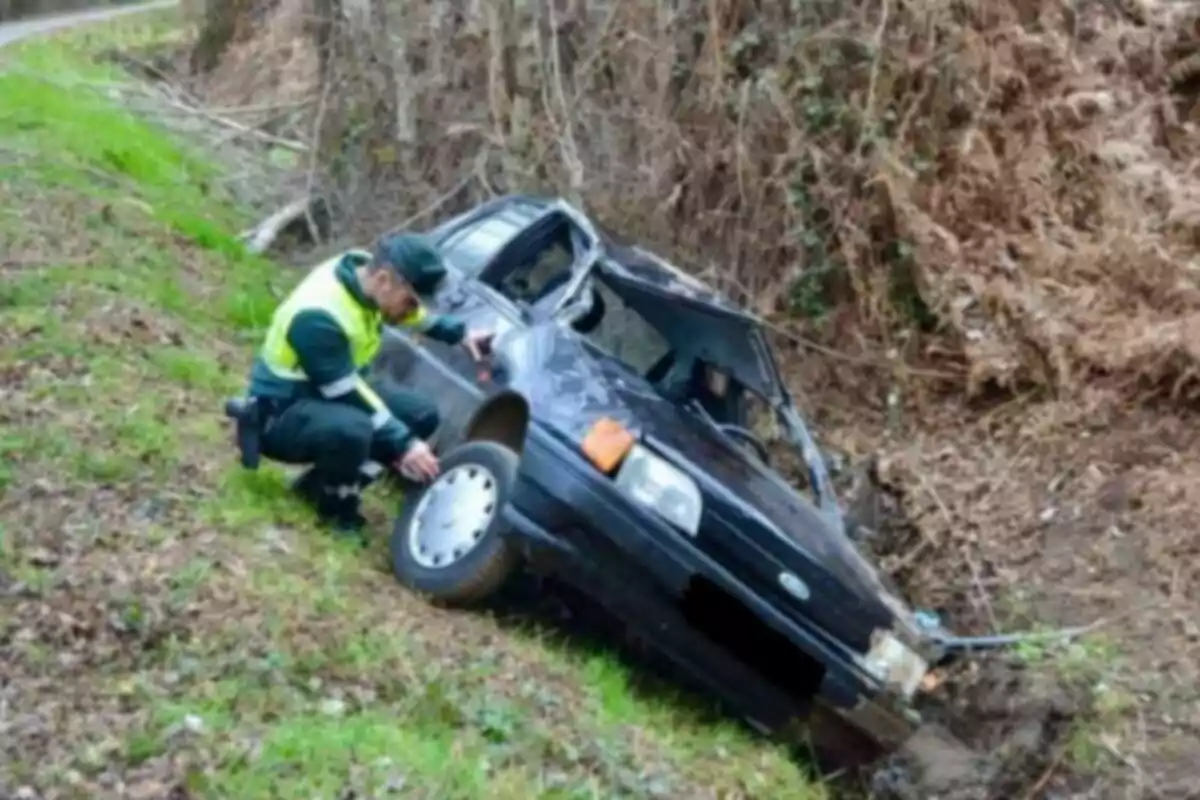 Un agent de trànsit inspecciona un cotxe accidentat en una rasa al costat d?un camí rural.