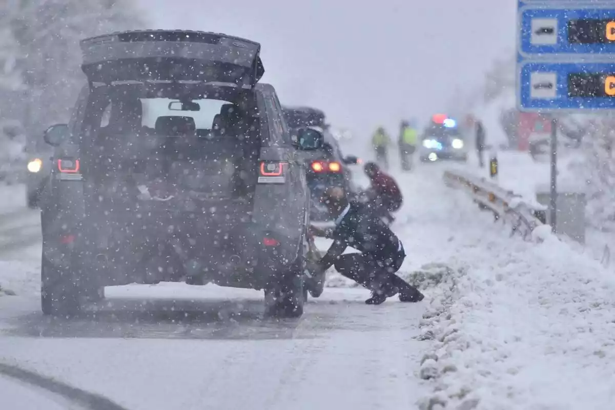 Diversos conductors col·locant cadenes a les rodes enmig d'una nevada intensa